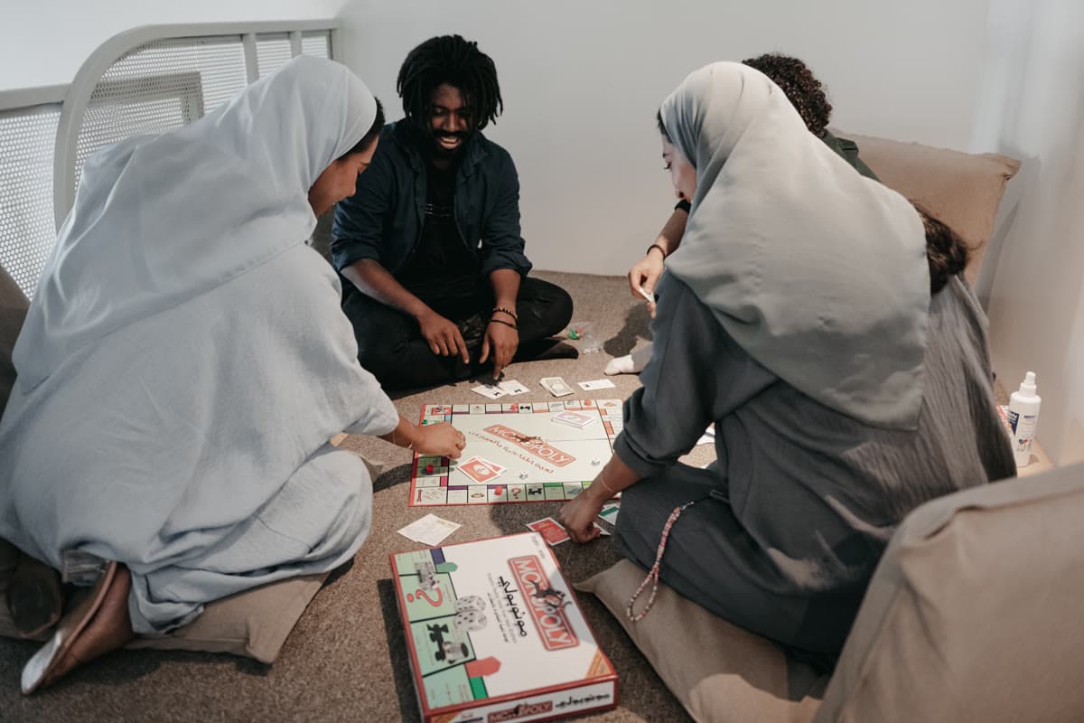 أربعة أشخاص يجلسون على الأرض حول لعبة لوحية في أمسية مجتمعية بمزج
